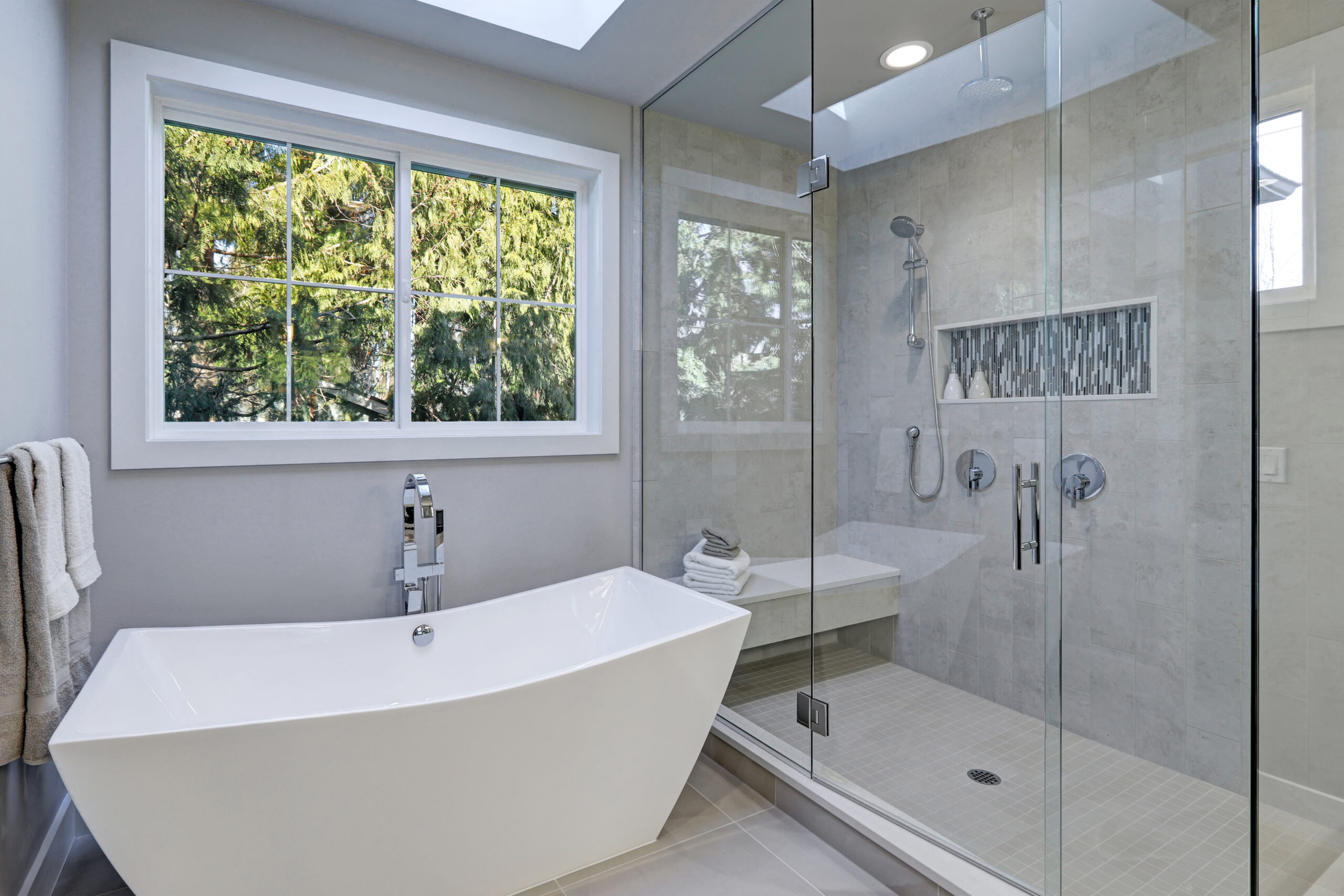 Glass walk-in shower with gray subway tiled surround and white freestanding tub in new luxury home bathroom. Northwest, USA