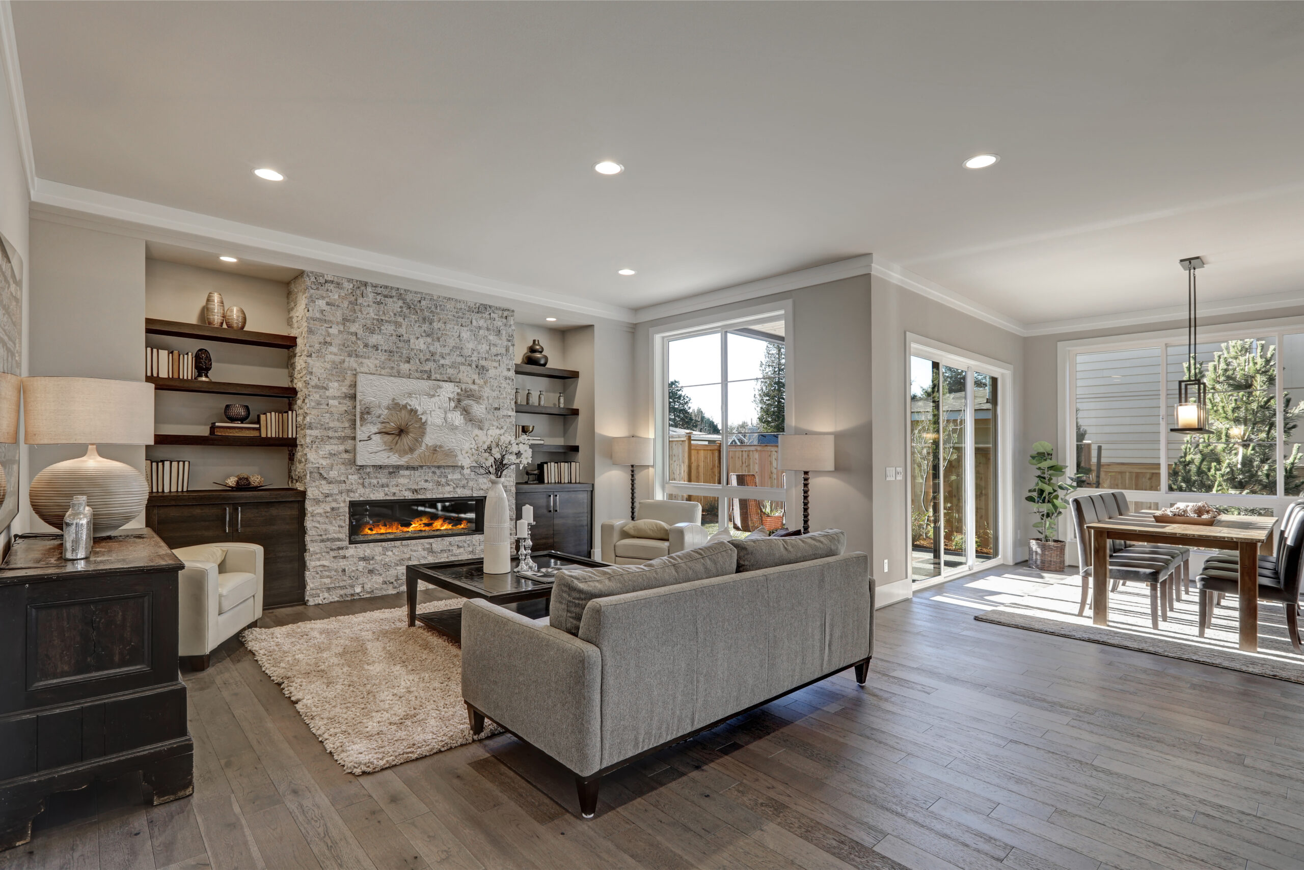 Living room interior in gray and brown colors features gray sofa atop dark hardwood floors facing stone fireplace with built-in shelves. Northwest, USA