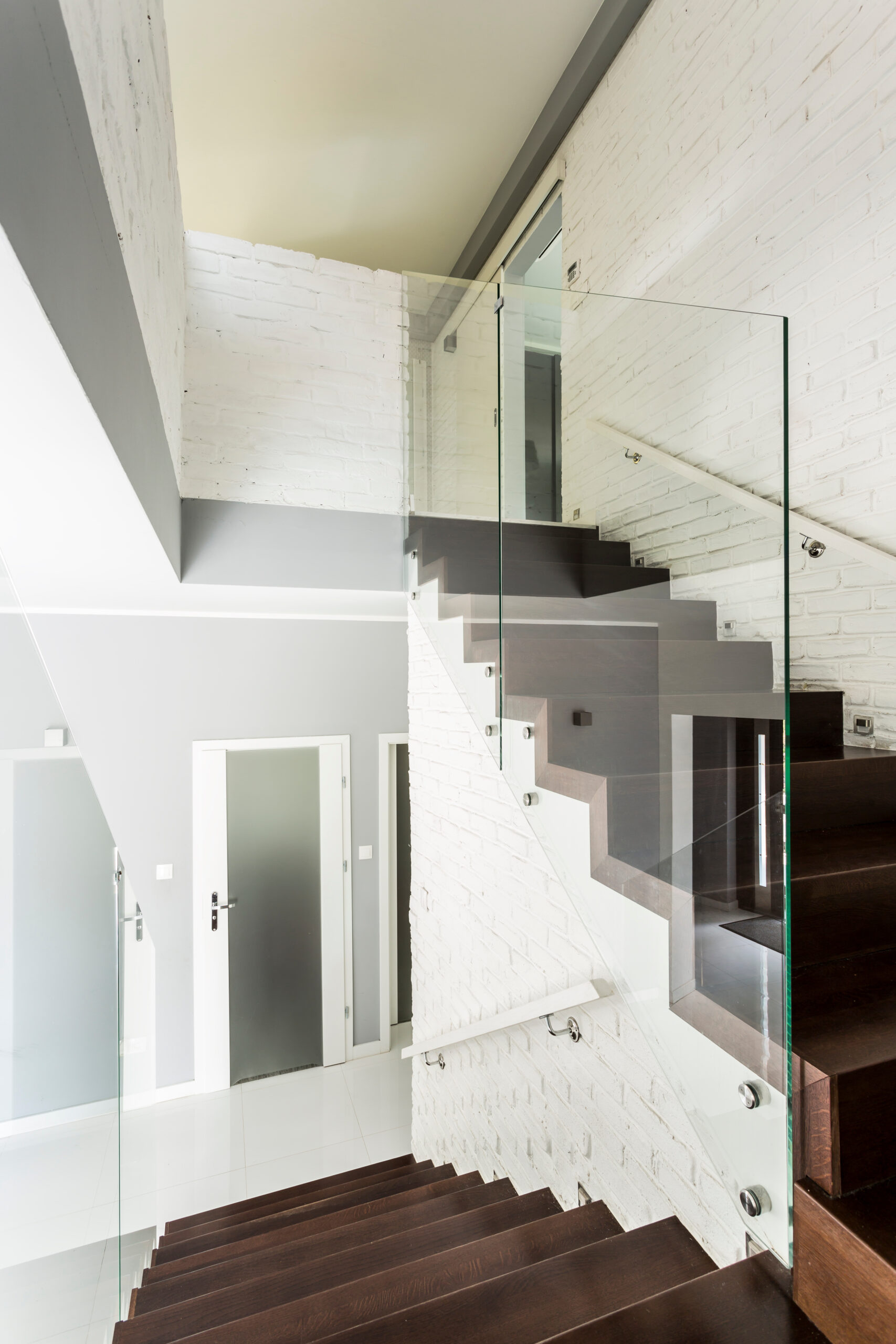 White staircase with wooden stairs, glass balustrade and chromed railing