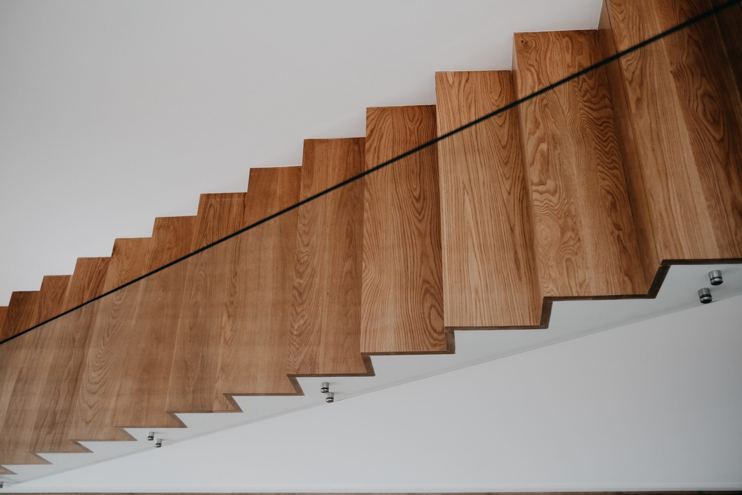 A high angle shot of a wooden staircase with glass railing inside a modern apartment