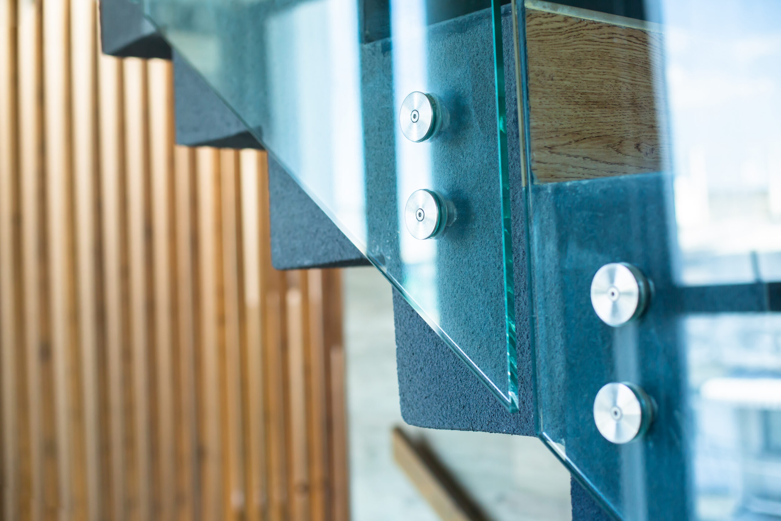 Selective focus to stainless steel bolts fixing glass to the stairs of modern buildings.