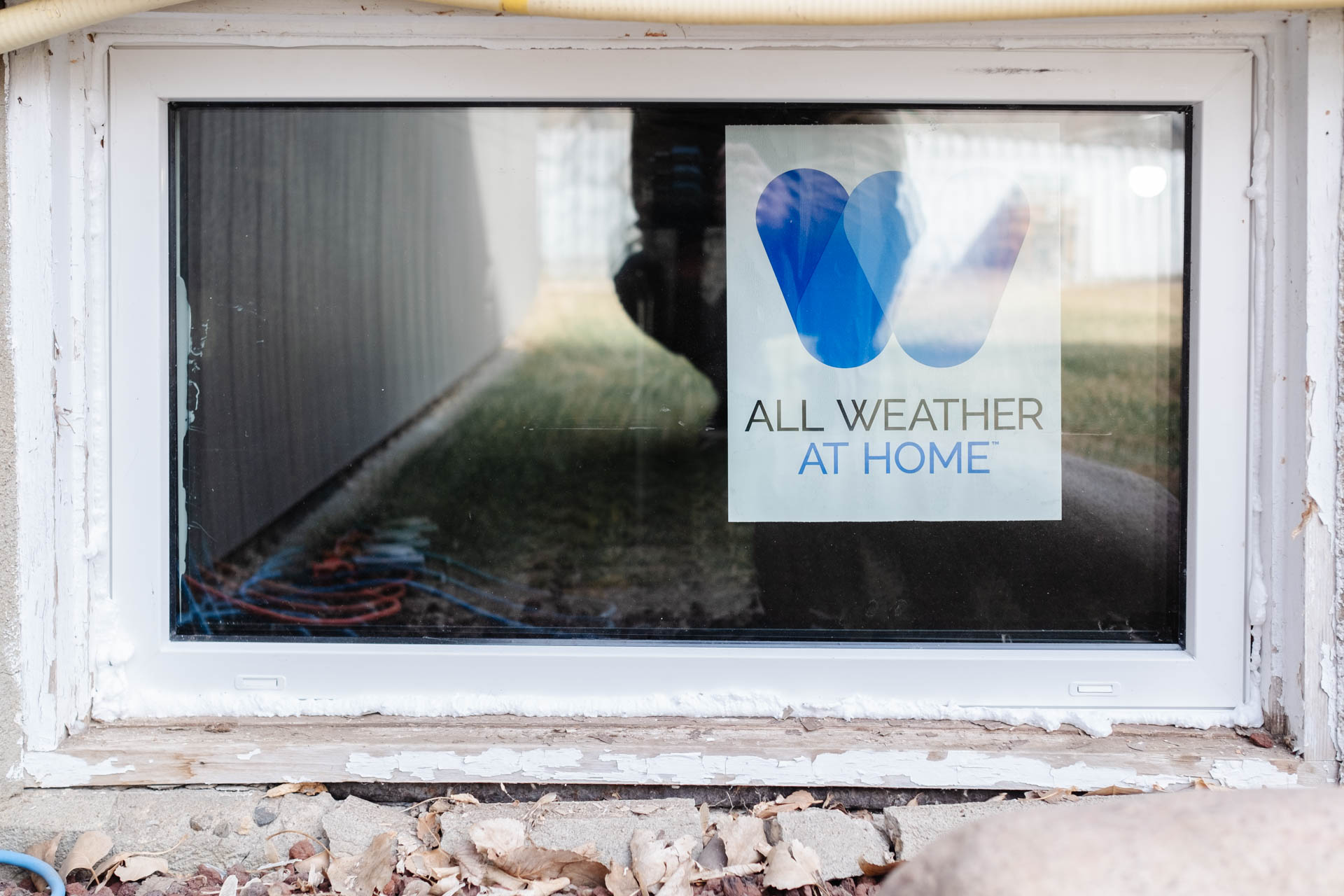 Freshly installed All Weather basement window with visible spray foam insulation around the edges.