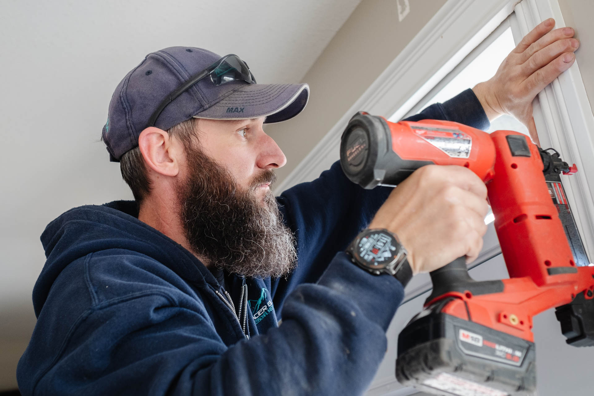 GG_04.21 (102) Glacier Glass employee installing trim on a newly installed white door. Holding an orange nail gun