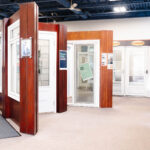This image presents a well lit interior view of a showroom displaying various residential windows and doors mounted in wooden frames, with a Glacier branded reception counter on the left and Larson branded products in the background. Glacier_Glass_Regina Glacier_Glass_Regina Glacier_Glass_Regina Glacier_Glass_Regina Glacier_Glass_Regina Glacier_Glass_Regina Glacier_Glass_Regina Glacier_Glass_Regina Glacier_Glass_Regina Glacier_Glass_Regina Glacier_Glass_Regina