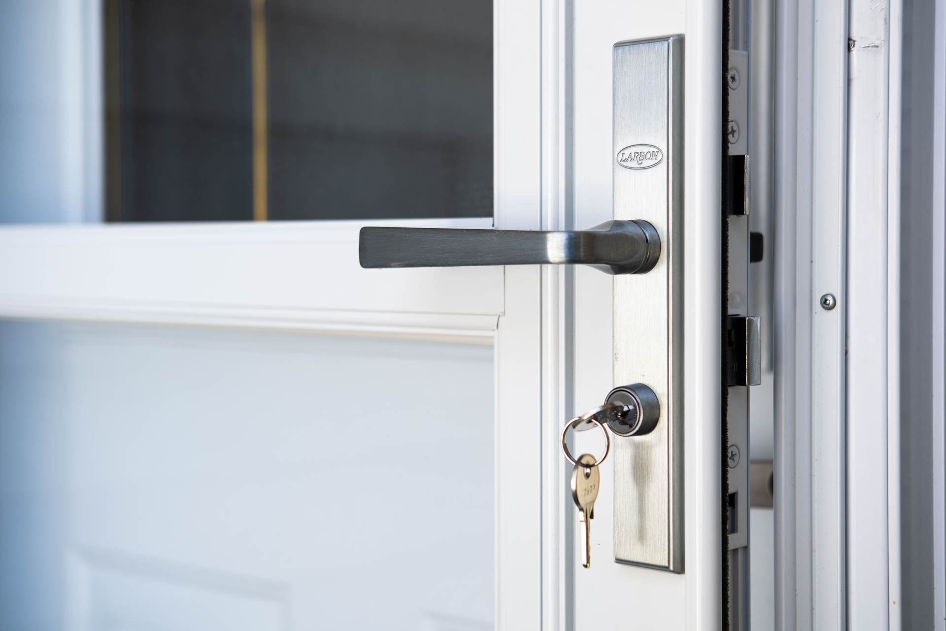 A slightly open white door with a silver handle and keys in the lower lock reveals a window through its upper panel. Glacier_Glass_Regina