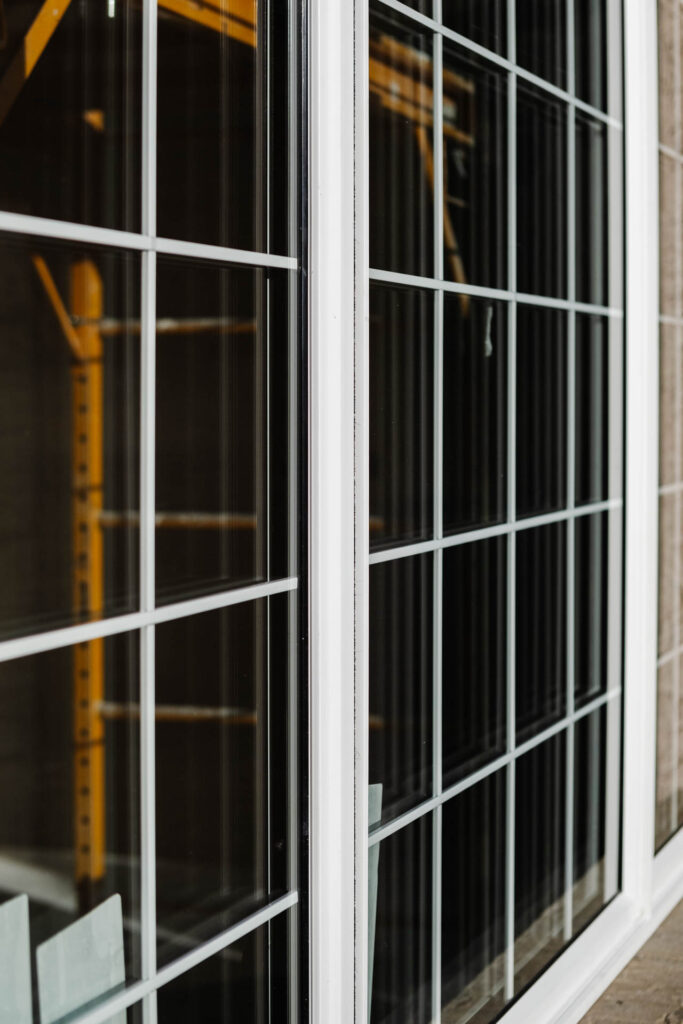 The image shows a close up of white gridded windows reflecting a yellow construction scaffold. Glacier_Glass_Regina