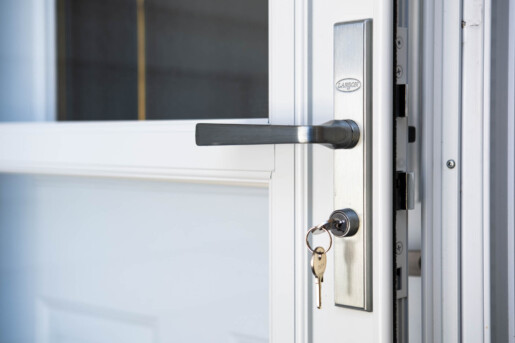 A set of keys hangs from a brushed metal lock and lever handle on a white door that is slightly ajar. Glacier_Glass_Regina